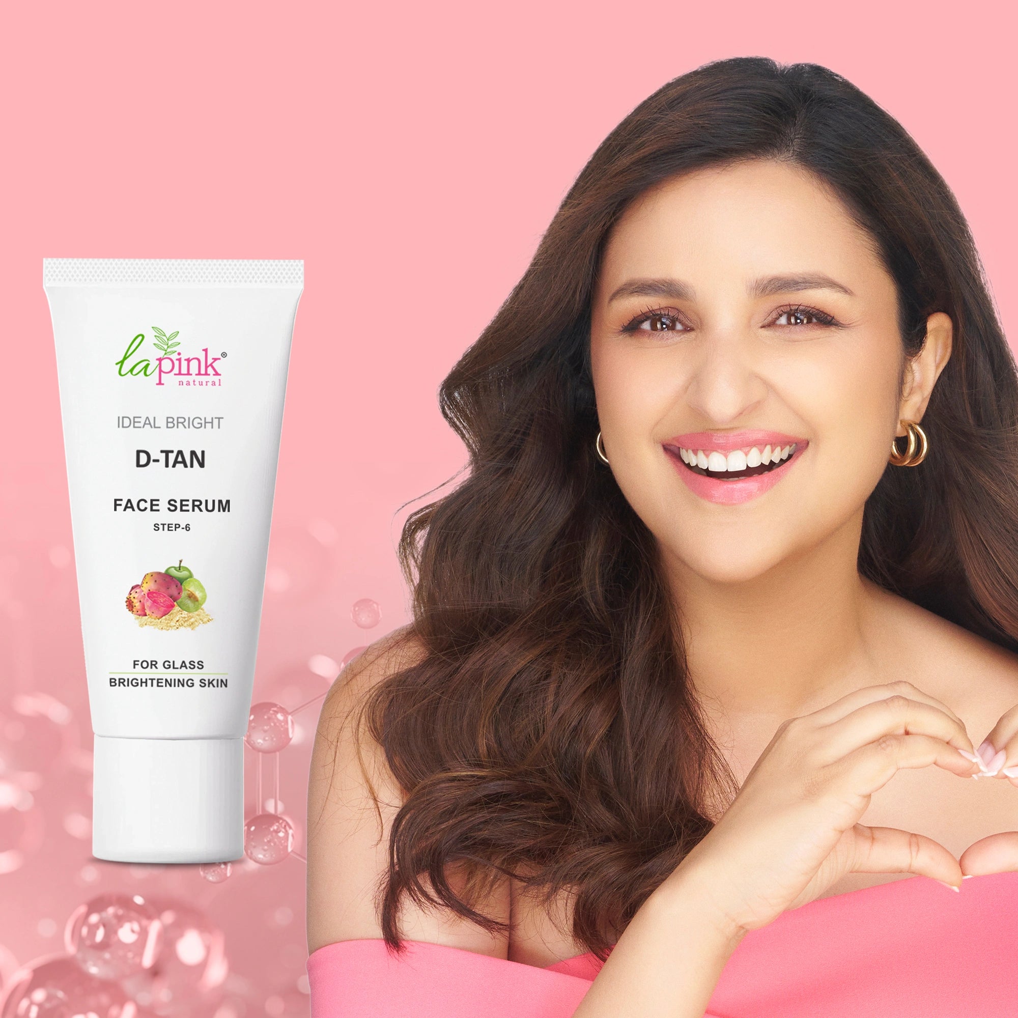 Woman with a heart gesture next to a tube of La Pink Ideal Bright D-Tan Face Serum on a pink background