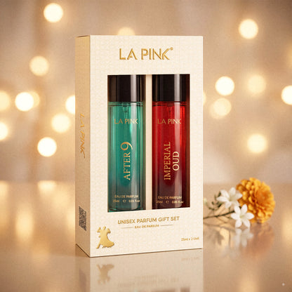 LA PINK Unisex Parfum Gift Set featuring a cream-colored box with two bottles, one green/teal and one red, displayed against a warm bokeh background with decorative flowers.

