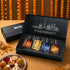 LA PINK Luxury Parfum Collection gift set in an open black presentation box, featuring four miniature glass perfume bottles with amber, gold, blue, and orange liquids. The set is styled on a warm beige surface with decorative marigold garlands and sweets in the background.


