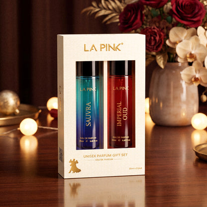 LA PINK Unisex Parfum Gift Set containing Sauvage and Imperial Oud, presented in a cream-colored box with gold lettering, set against a warm, softly lit background with flowers and bokeh lights.

