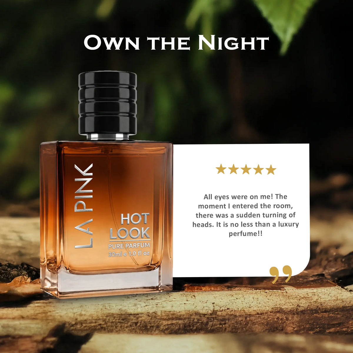 LA PINK Hot Look Eau de Parfum bottle shown next to a white promotional card with a five-star review, set on a rustic wooden surface with a dark, blurred forest background.

