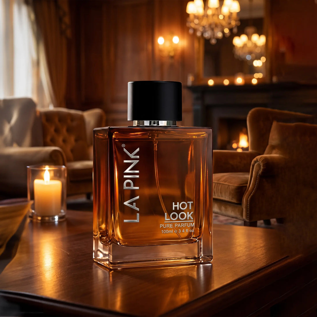 A bottle of LA PINK Hot Look Pure Parfum with amber liquid and a black cap, displayed on a wooden table in a warm, elegant room with a lit candle and chandeliers in the background.

